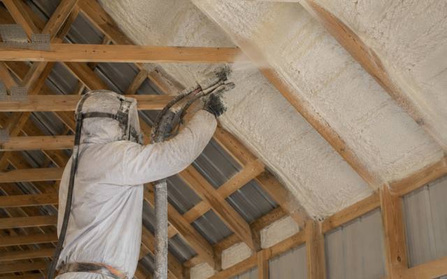 Installer spraying the roof deck of a steel-clad barn